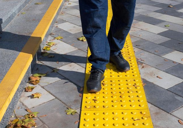 imagem de uma pessoa andando em uma calçada de concreto com faixa de piso tátil 